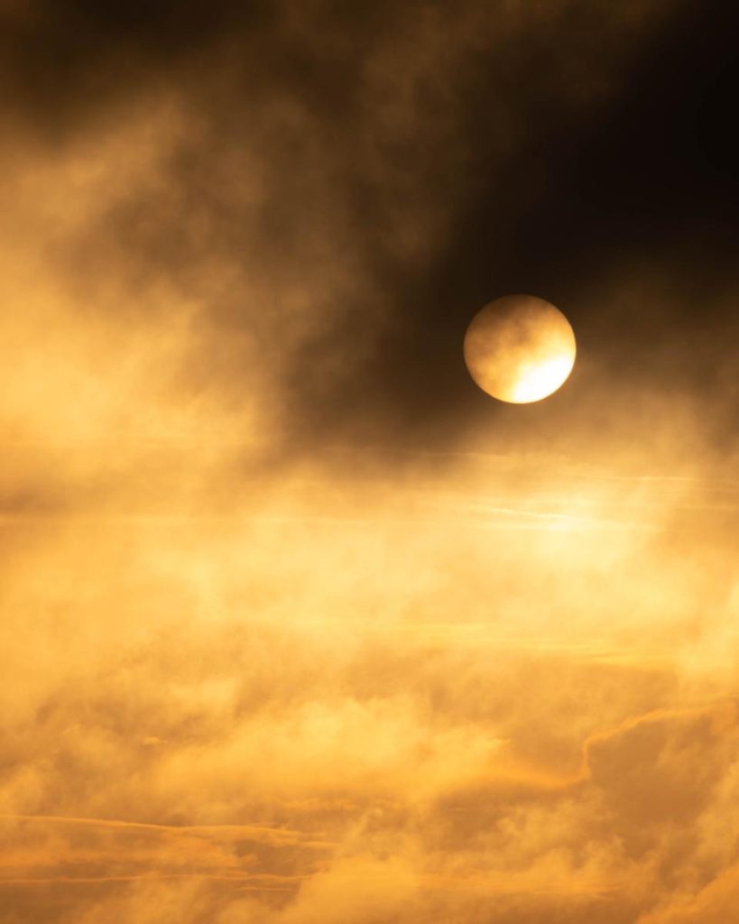 Satured, gold skies contrast with dark black clouds that flash over the sun, giving the illusion of an eclipse