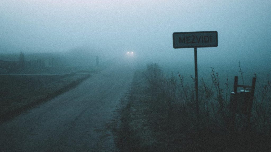 A thick blue mist is pierced by the headlights of a car near Valmiera