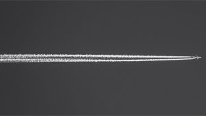 Black and white image of clear sky that is crossed by the airoplane and it's trailing tail